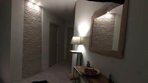 Un pasillo con pared de ladrillo, un espejo, una lámpara y una mesita con un cuenco.