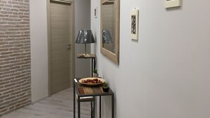 Un pasillo con una puerta de madera, una mesa pequeña con un cuenco de comida, una lámpara y cuadros en la pared.