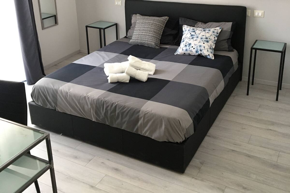 Un dormitorio moderno con una cama grande, dos mesitas de noche, un espejo y dos lámparas de pared.
