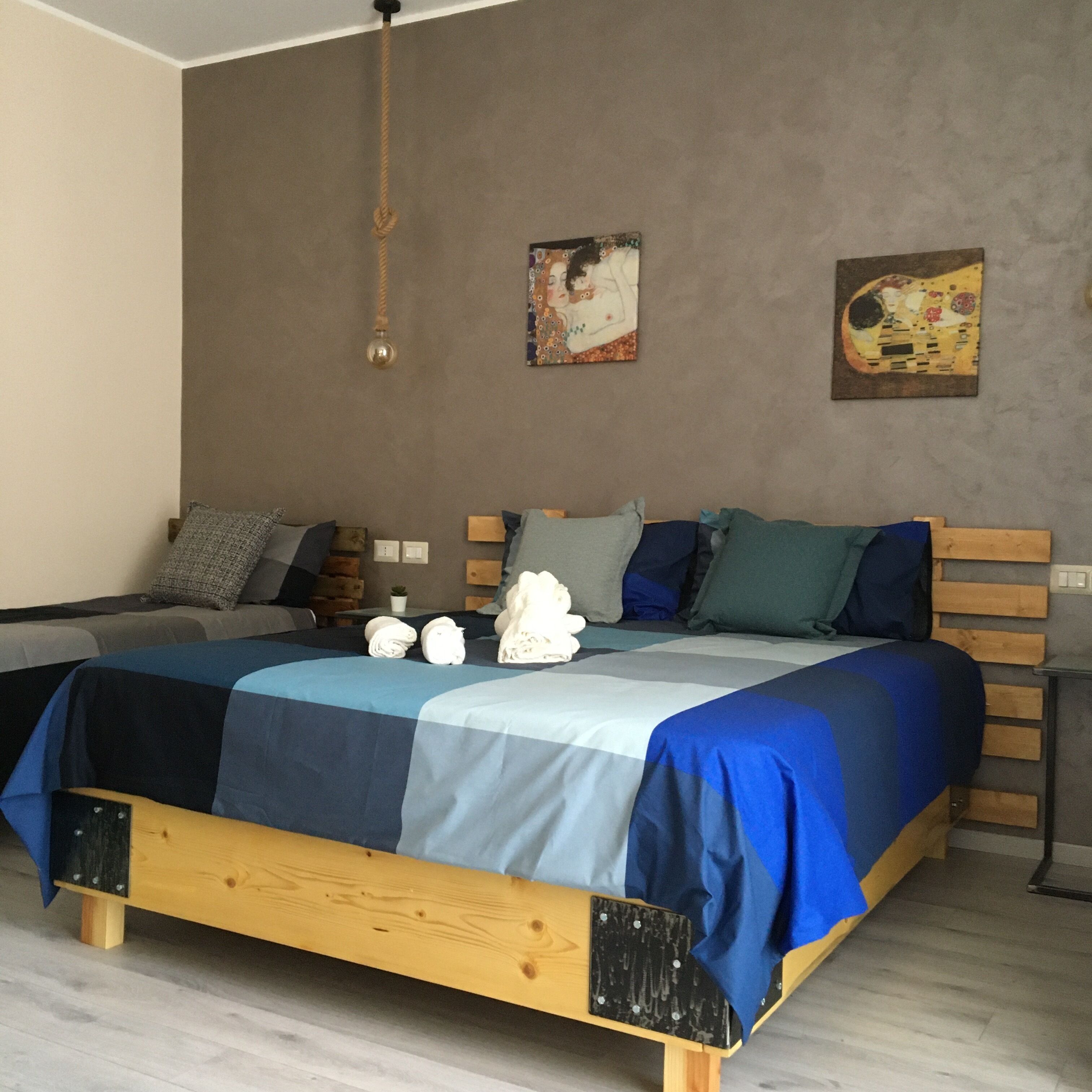 Une chambre à coucher moderne avec un cadre de lit en bois, une literie bleue et grise, et deux œuvres d’art murales.