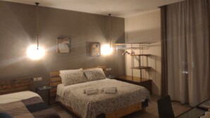 Un dormitorio con cama, mesitas de noche, lámpara colgante y ventana con cortinas.