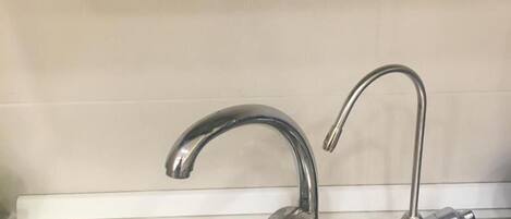 A kitchen sink with two faucets, a stainless steel basin, and a tiled backsplash.