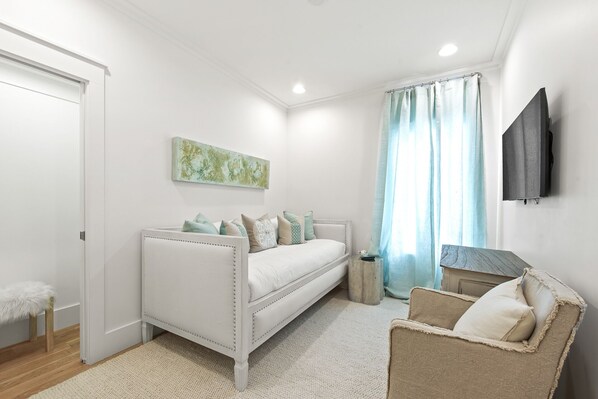 Une chambre à coucher avec un lit, une chaise, une petite table, un tableau et une fenêtre avec des rideaux.