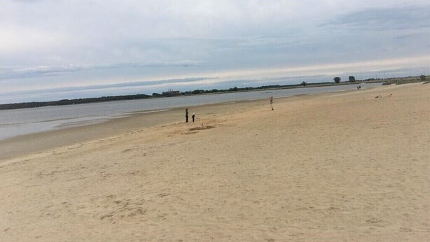 Ein weiter Sandstrand mit ruhiger See und bewölktem Himmel.