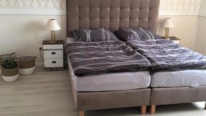 Ein Schlafzimmer mit einem bettgestelltem Bett, zwei Nachttischen mit Lampen, einem kleinen Nachttisch mit einer Lampe und einer Topfpflanze.