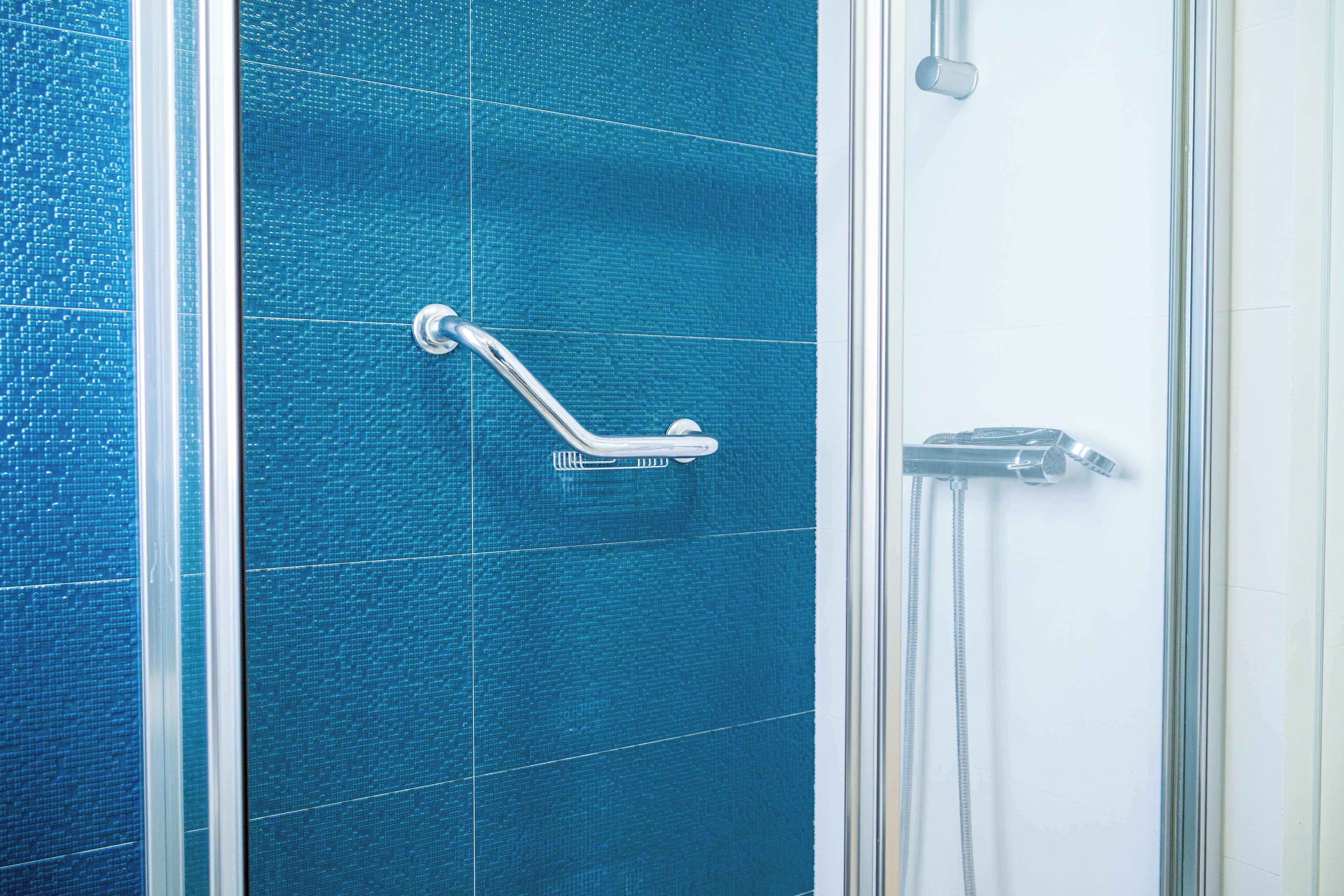 Ein Badezimmer mit blauen Fliesen, einer Duschkabine aus Glas und einer Handstange.