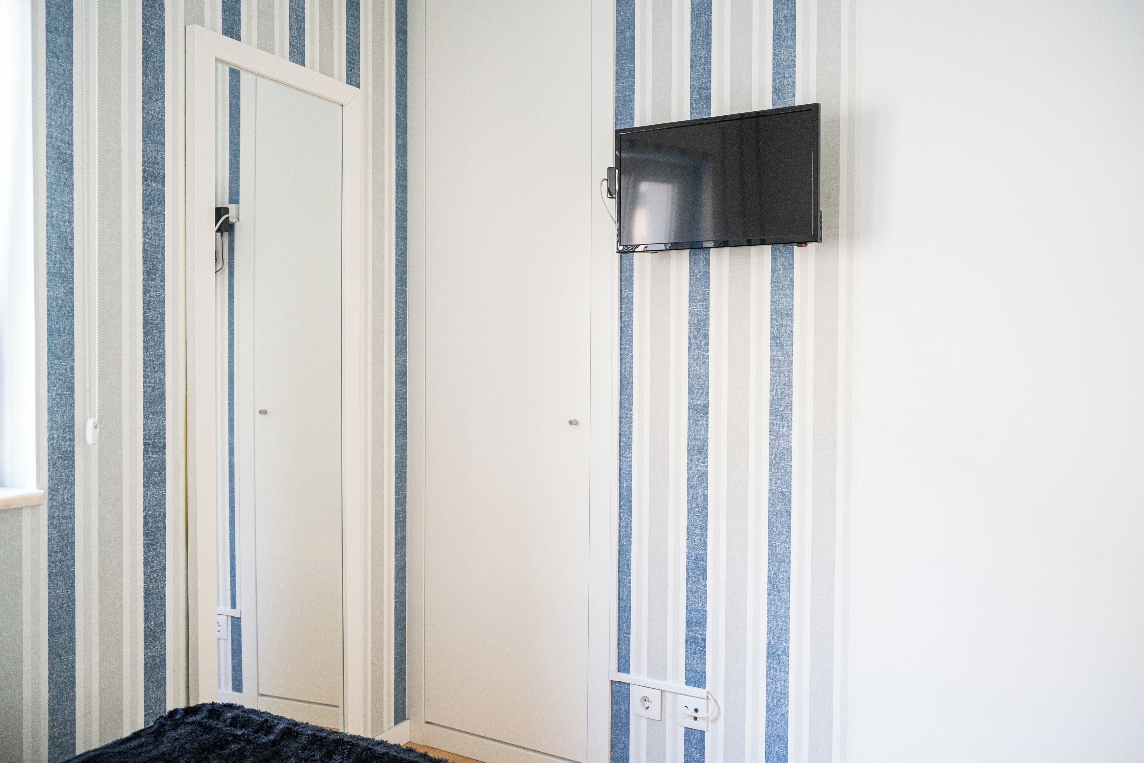 A room with striped wallpaper, a white door, and a mounted flat-screen TV.