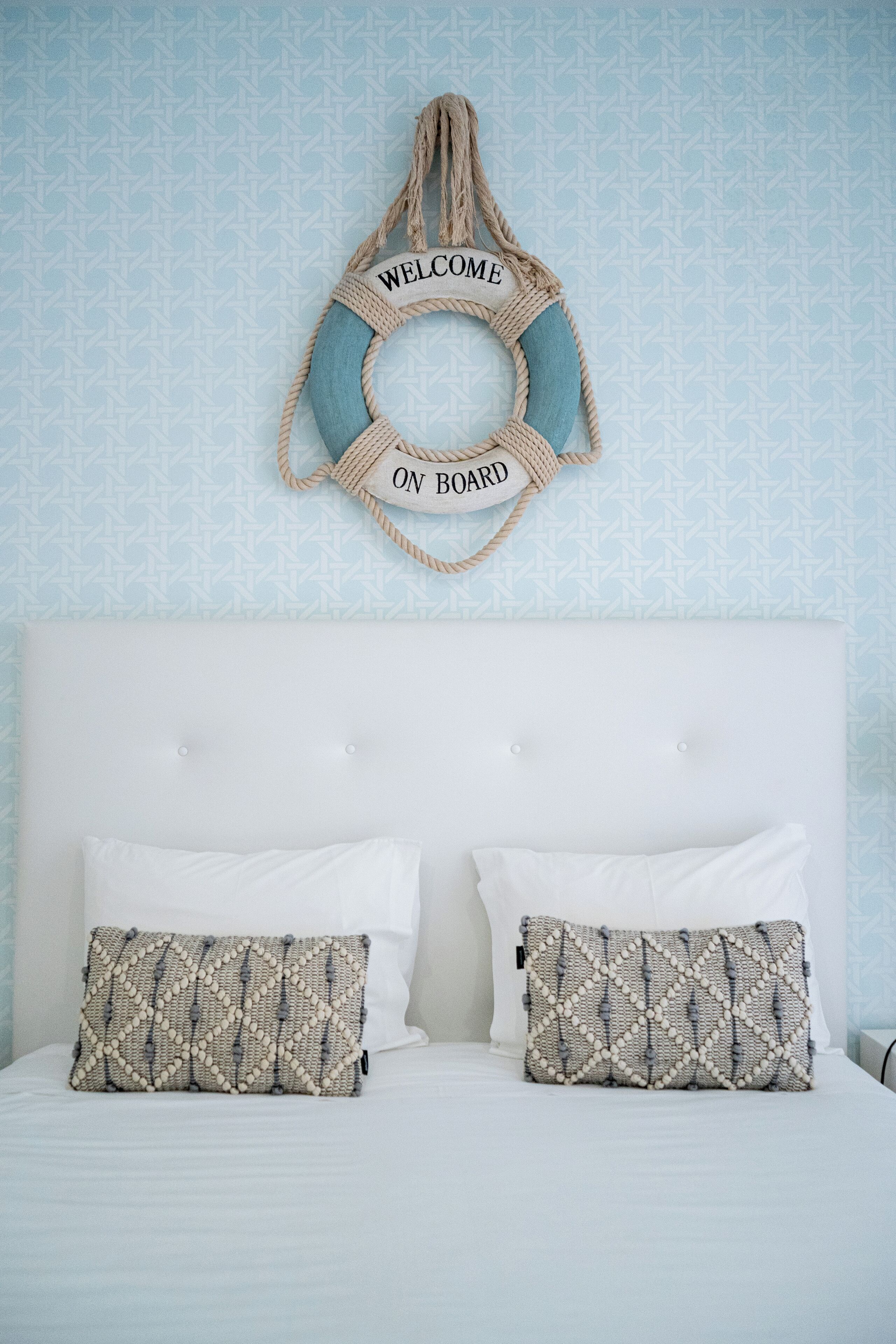 A bed with two pillows, a white headboard, and a wall with a blue patterned wallpaper.