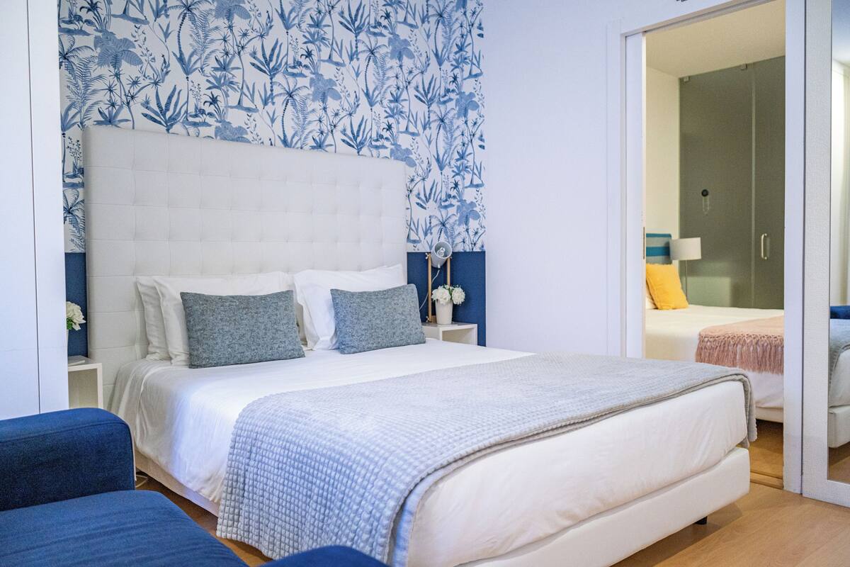 A bedroom with a large bed, a nightstand, a blue chair, and a wardrobe.