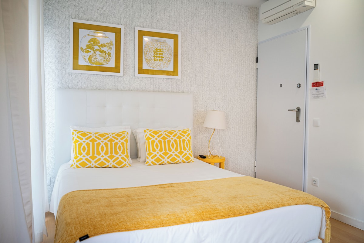 A hotel room with a bed, two framed pictures on the wall, a bedside lamp, and a door with a sign.