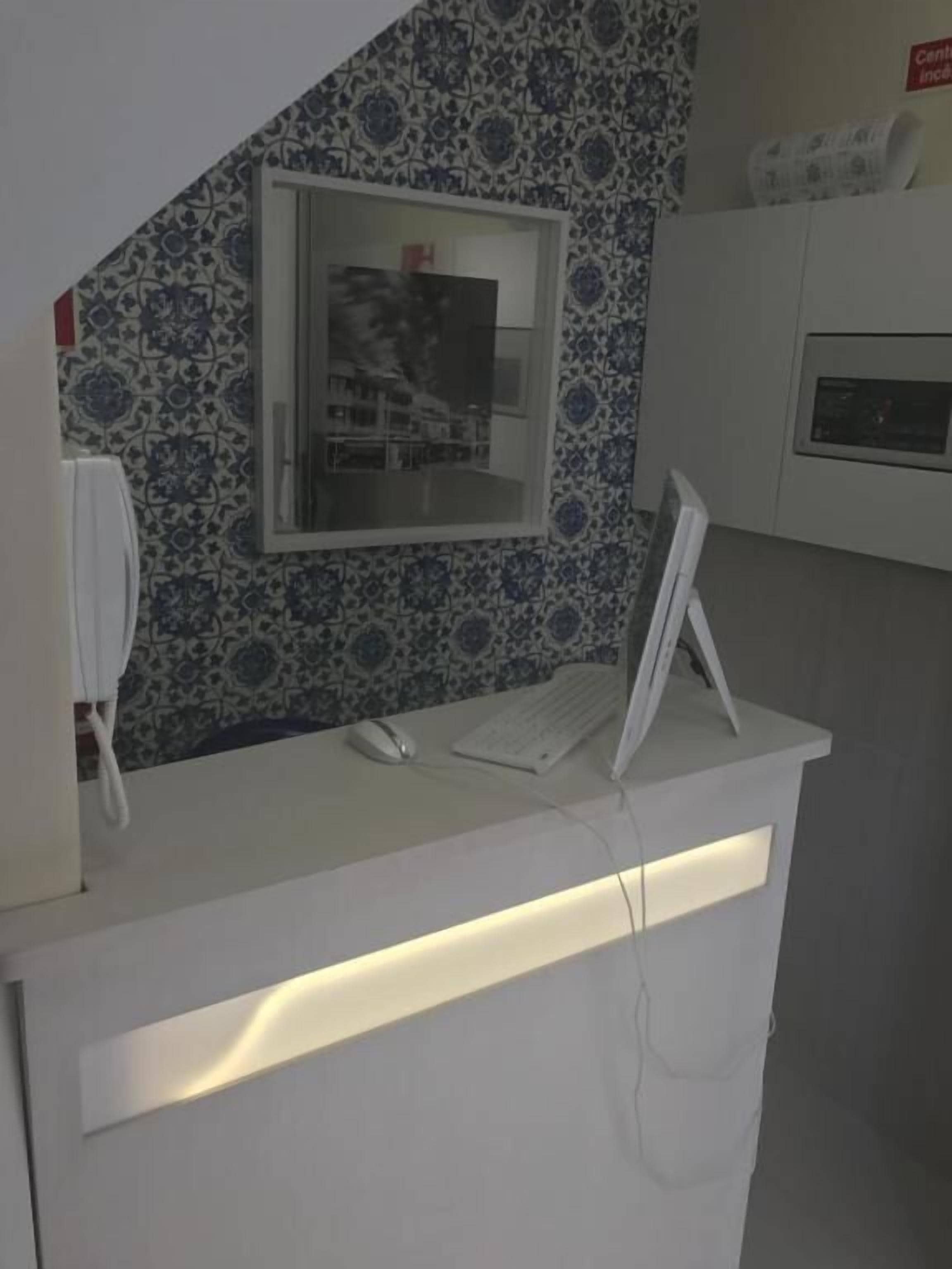 A reception desk with a computer monitor, keyboard, and mouse. There is a telephone on the left and a window with a view of buildings.