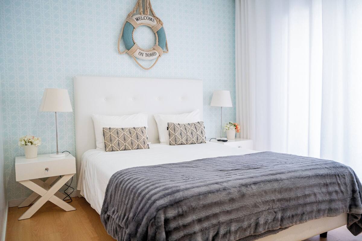 A neatly arranged bedroom with a white headboard, two bedside tables with lamps, and a grey blanket.