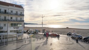 A coastal building with a restaurant named "Restaurant Mar Bravo" and a parking area with cars and a truck. - By The Sea  (Nazaré)