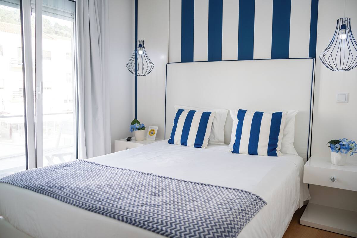A modern bedroom with a large bed, striped pillows, and a patterned throw.