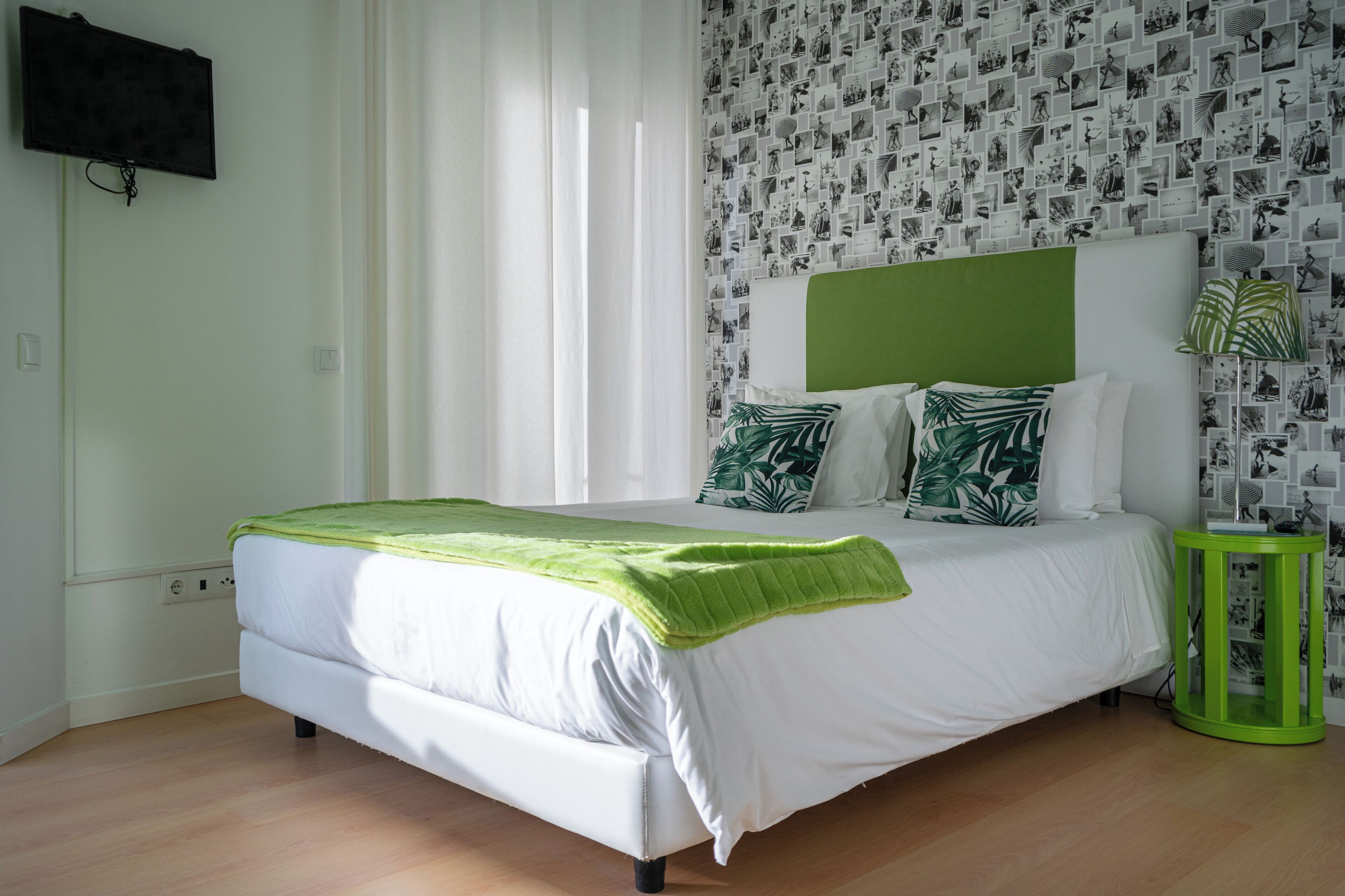 A neatly made bed with a green headboard and white bedding, a green side table, and a wall with a patterned wallpaper.