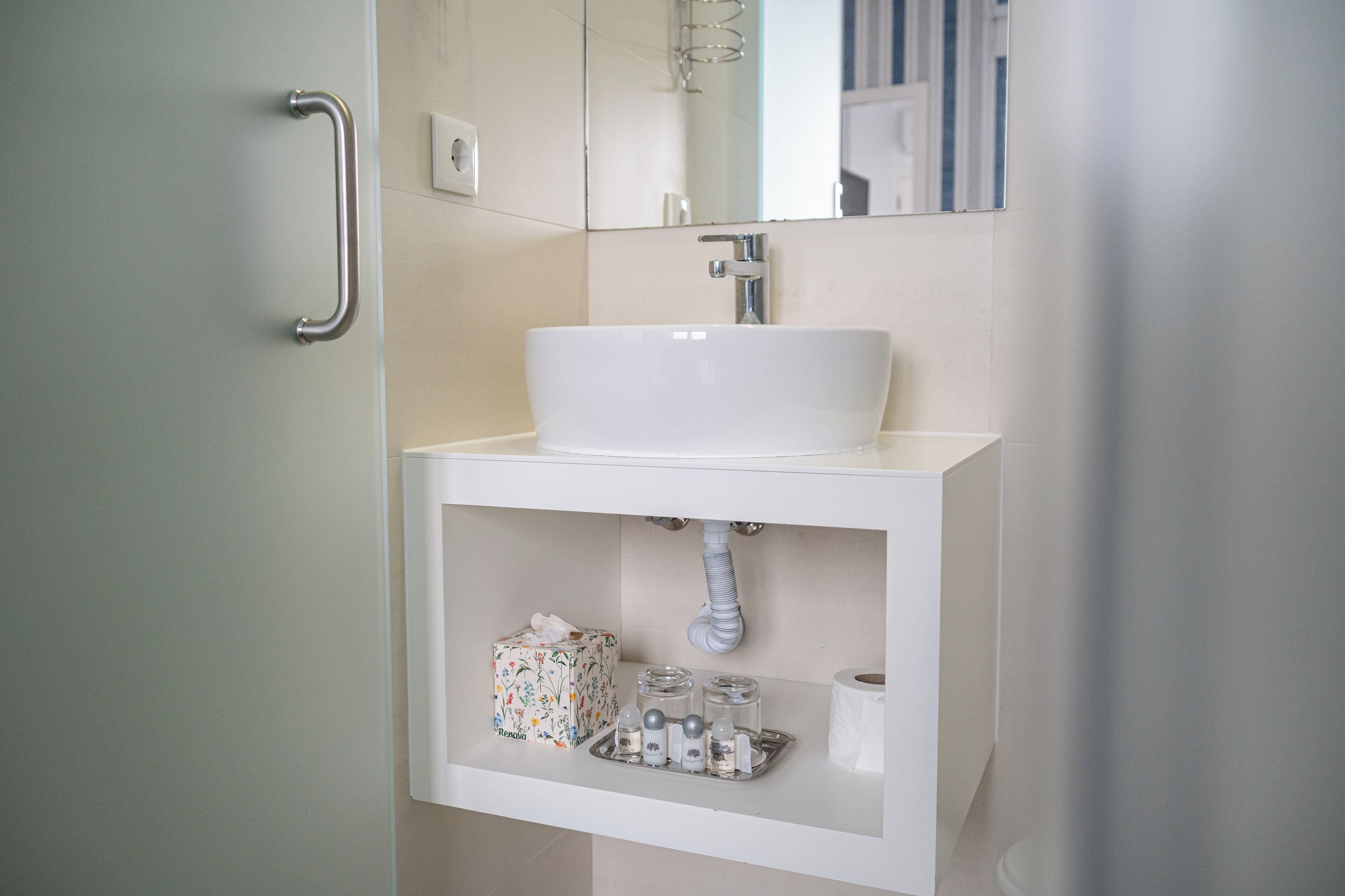 A bathroom with a white sink, a handrail, a mirror, and a shelf with toiletries.