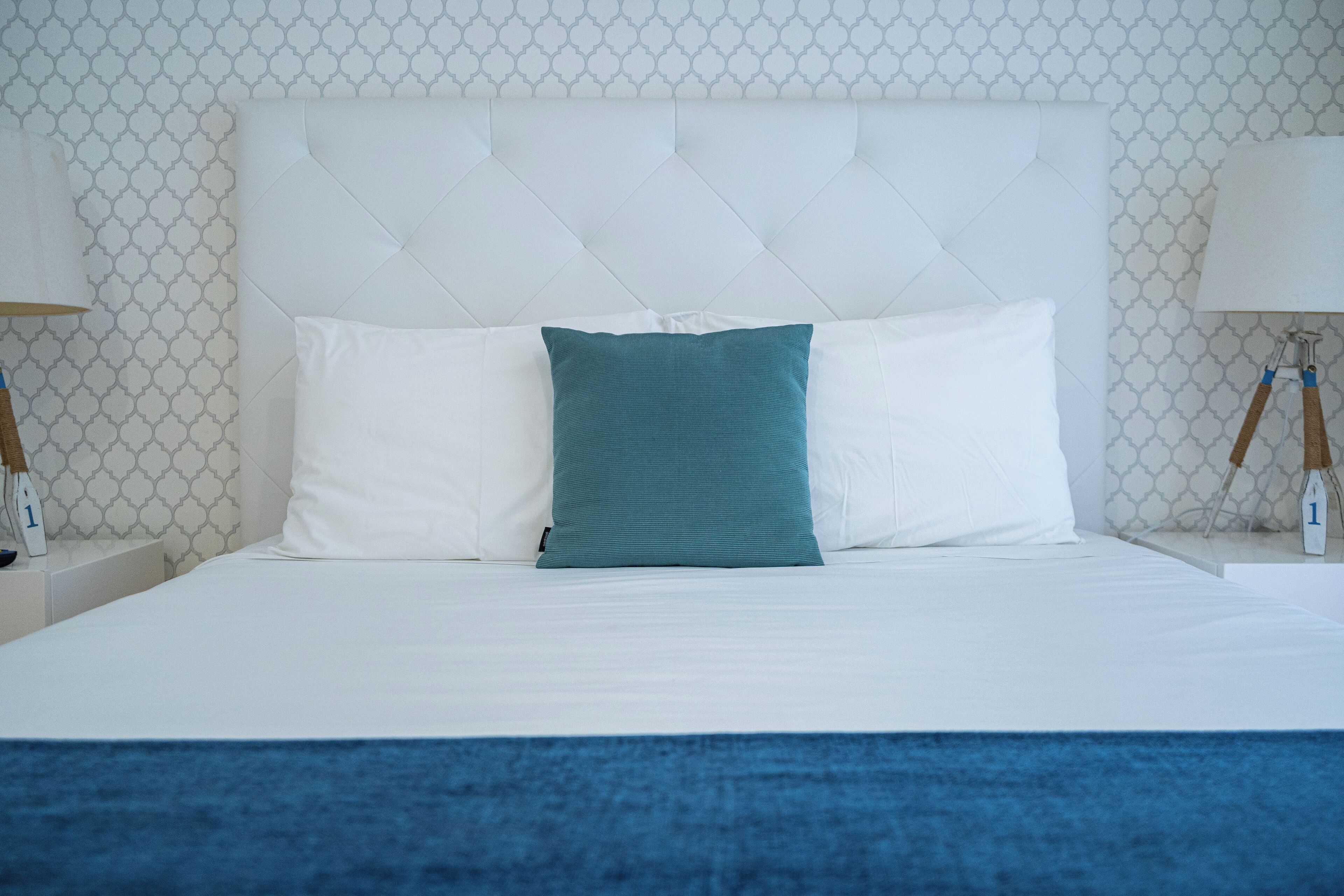 Una cama con ropa de cama impecable, almohadas blancas y azul turquesa, y una manta azul.
