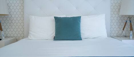Una cama con ropa de cama impecable, almohadas blancas y azul turquesa, y una manta azul.