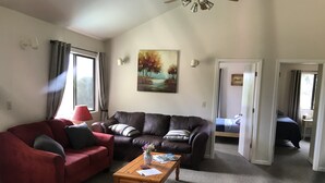A living room with a red sofa, a brown leather couch, and a wooden coffee table. There is a painting on the wall and a window with curtains. - The Terrace House, country living. (Montgomery Creek)