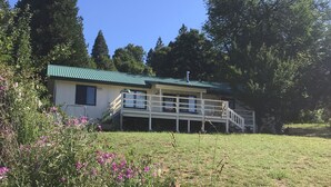 A two-story building with a green roof, surrounded by a grassy field and trees. - The Terrace House, country living. (Montgomery Creek)