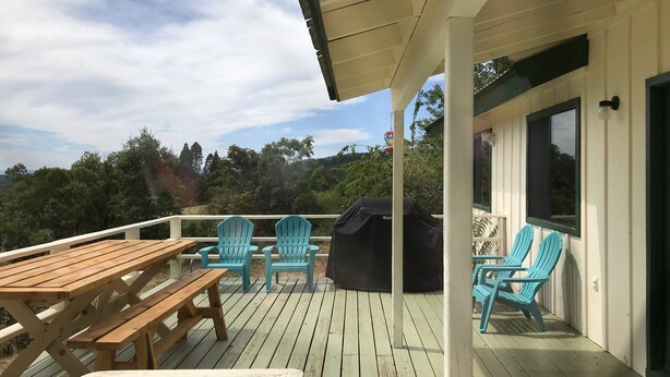 A wooden deck with picnic tables and chairs, a barbecue grill, and a view of the surrounding landscape. - The Terrace House, country living. (Montgomery Creek)