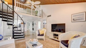 A spacious living area with a high ceiling, a staircase, a television, wicker furniture, and a white railing. - BT 3322 Fountain/Pond View Condo-Paradise Vacation Rental in Ocean Village (Fort Pierce)