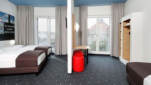 Una habitación de hotel con dos camas, un escritorio, un reposapiés rojo y un armario.