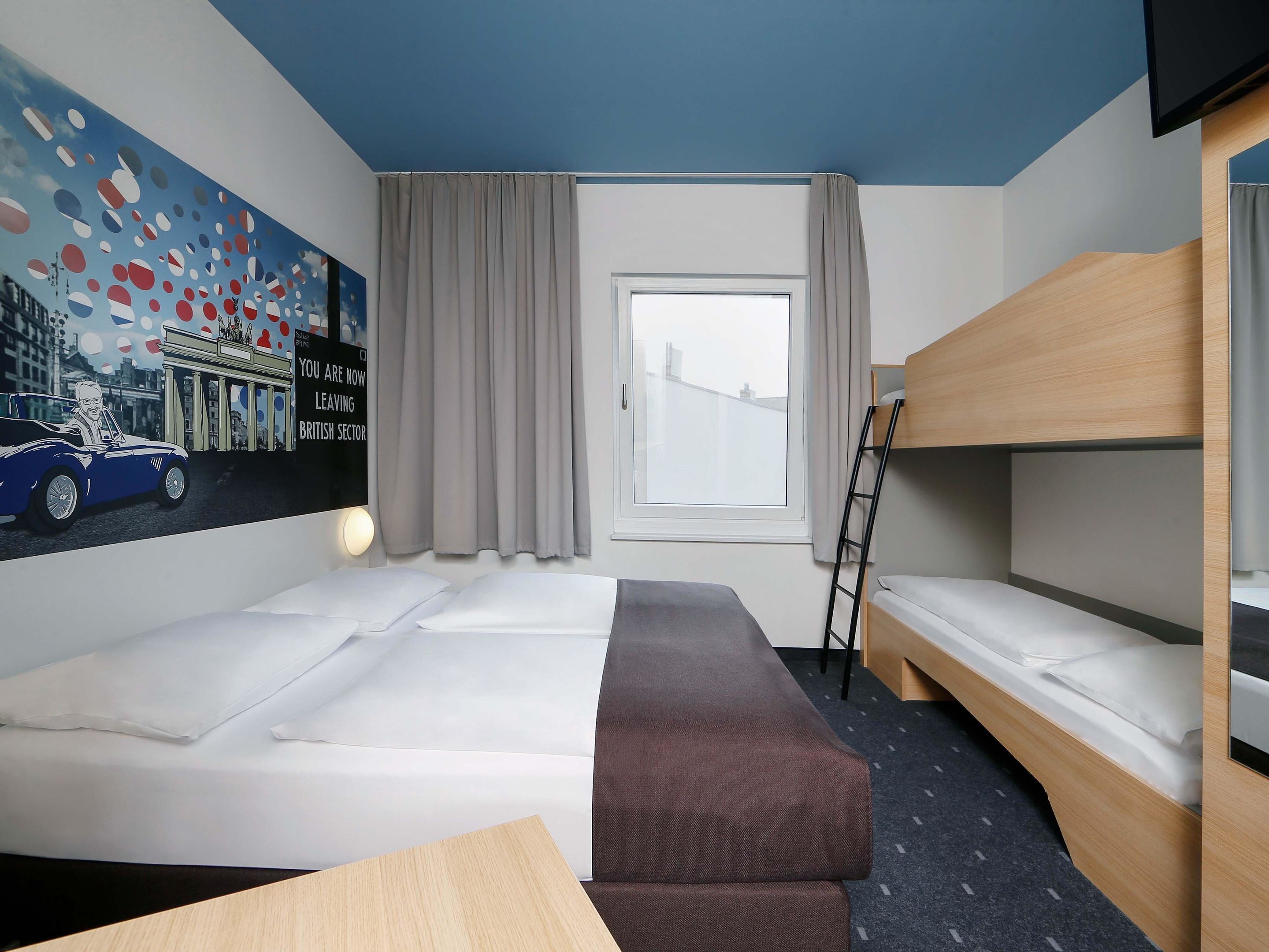 Habitación de hotel con literas, cama individual, escritorio y ventana con cortinas.