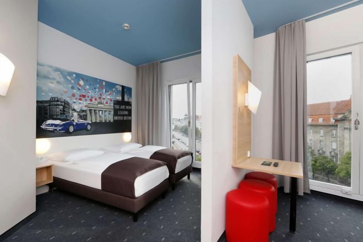 Una habitación de hotel con cama, escritorio y un amplio ventanal con vistas a la ciudad.