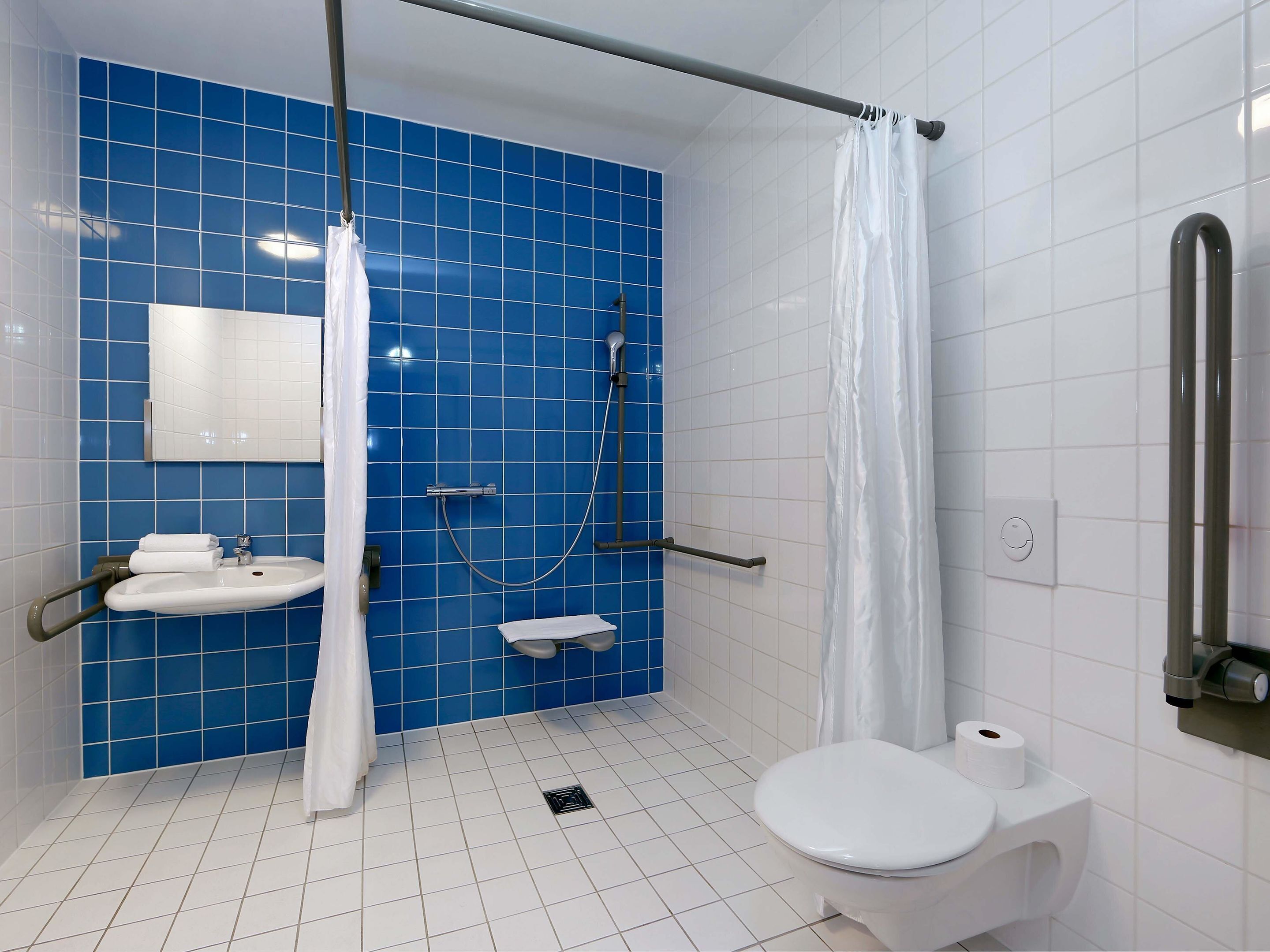 Ein Badezimmer mit blauen Fliesen, einem weißen Waschbecken, einer Toilette und einer Duschkabine mit Vorhang.