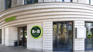 Entree van een B&B hotel met een receptie, een rond logo en een receptiebord.