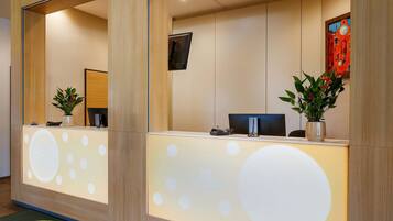 A reception desk with a modern design, featuring a large mirror, a digital screen, and potted plants.