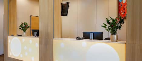 Un mostrador de recepción de diseño moderno, con un espejo grande, una pantalla digital y plantas en macetas.