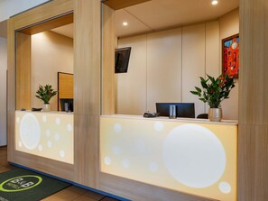 Un mostrador de recepción de diseño moderno, con un espejo grande, una pantalla digital y plantas en macetas.