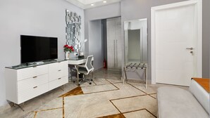A modern bedroom with a TV, white dresser, and a desk with a chair.