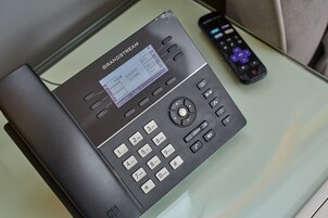 A black telephone with a display screen and keypad, placed on a glass table next to a remote control.