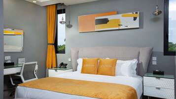 A modern hotel room with a large bed, a desk with a chair, a telephone, and a nightstand with a lamp.