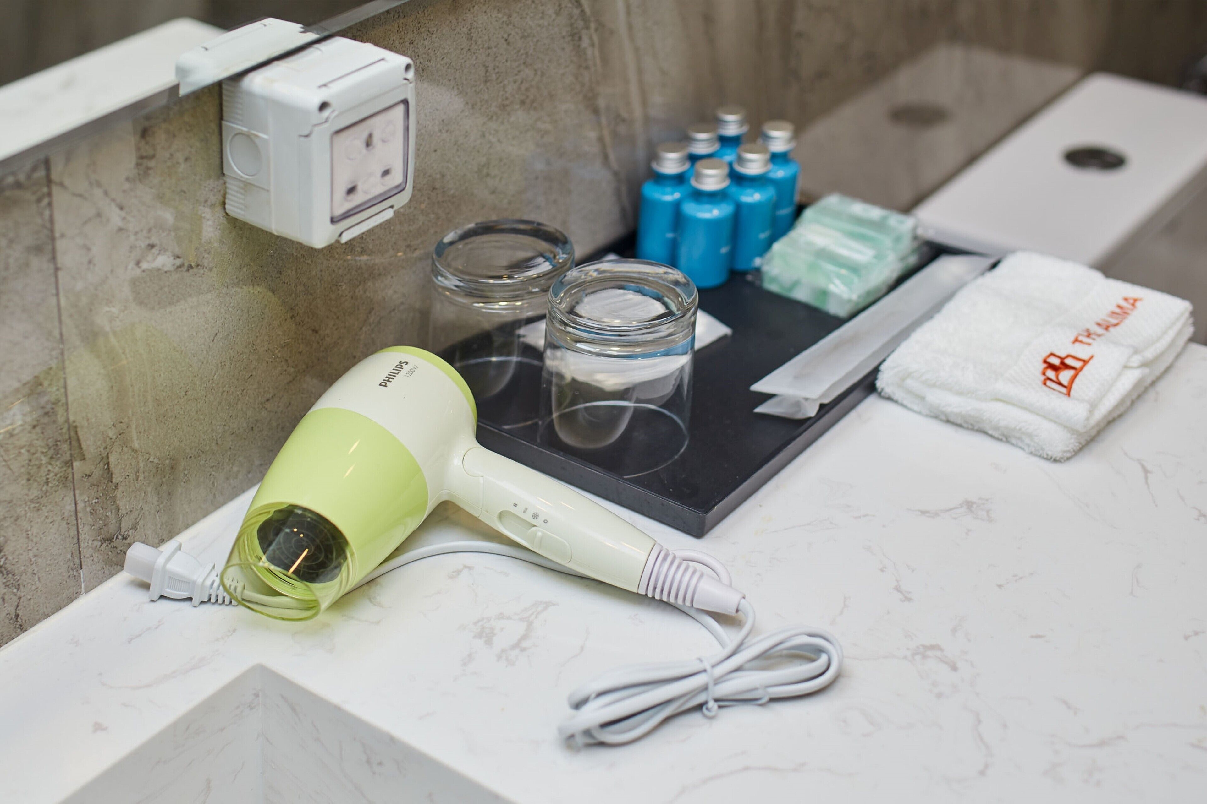 A bathroom counter with a hairdryer, glass jars, toiletries, and a towel.