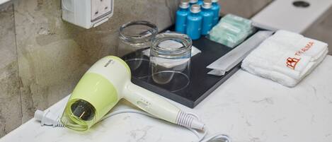 A bathroom counter with a hairdryer, glass jars, toiletries, and a towel.