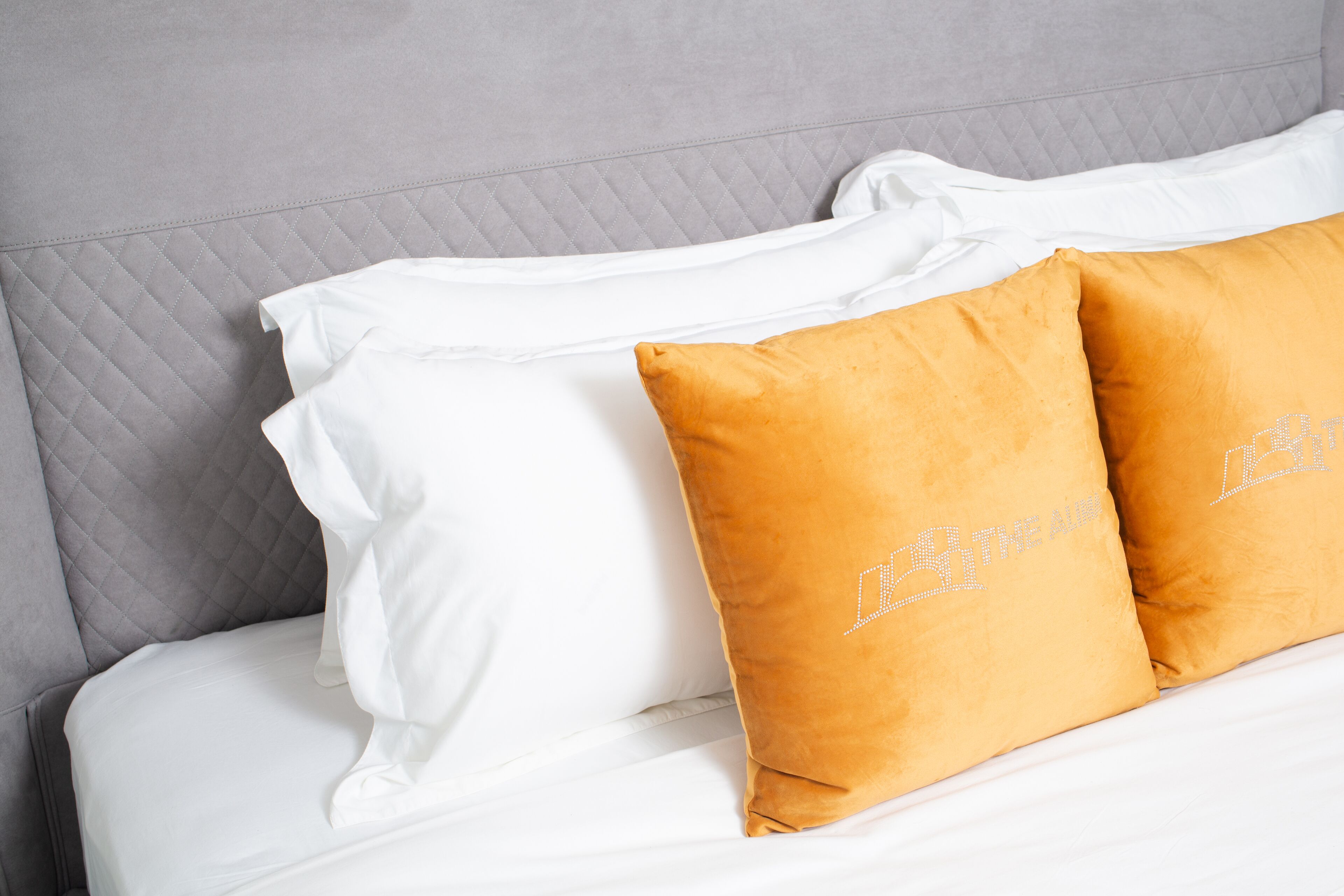 A bed with white bedding and two orange pillows.