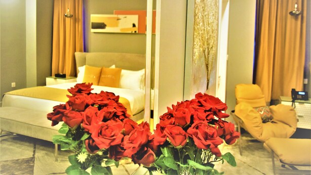 A hotel room with a bed, a sitting area, and a large mirror reflecting the room.