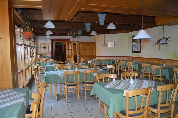 A dining area with multiple tables and chairs, wooden beams on the ceiling, and hanging pendant lights. - Gasthof Zahler (Röfingen)