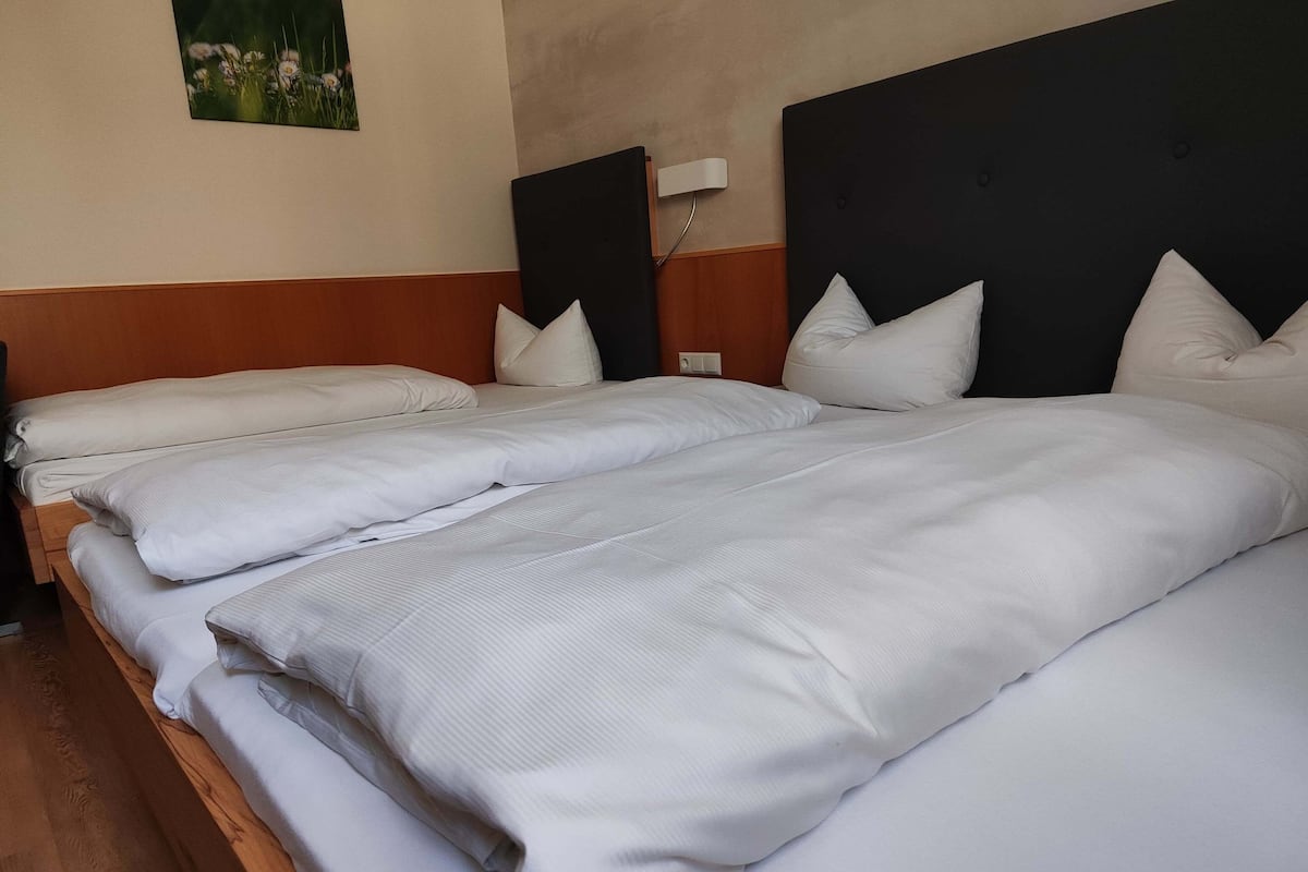 Un lit jumeau bien fait, avec du linge de lit blanc et une tête de lit en bois.