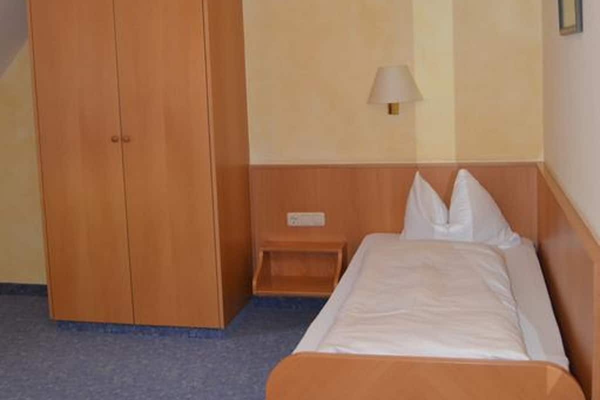 Une chambre d’hôtel avec un lit, une armoire en bois, une table de chevet et une lampe fixée au mur.