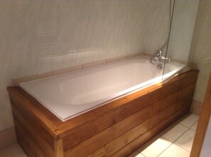 A wooden bathtub with a glass enclosure, a faucet, and a showerhead.