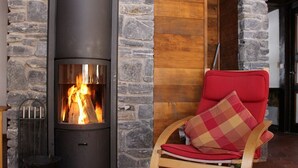 A stone fireplace with a fire, a rocking chair with a red cushion, and a wooden door.