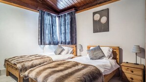 A double bed with a fur throw, a wooden headboard, a nightstand with a lamp, and a window with curtains.
