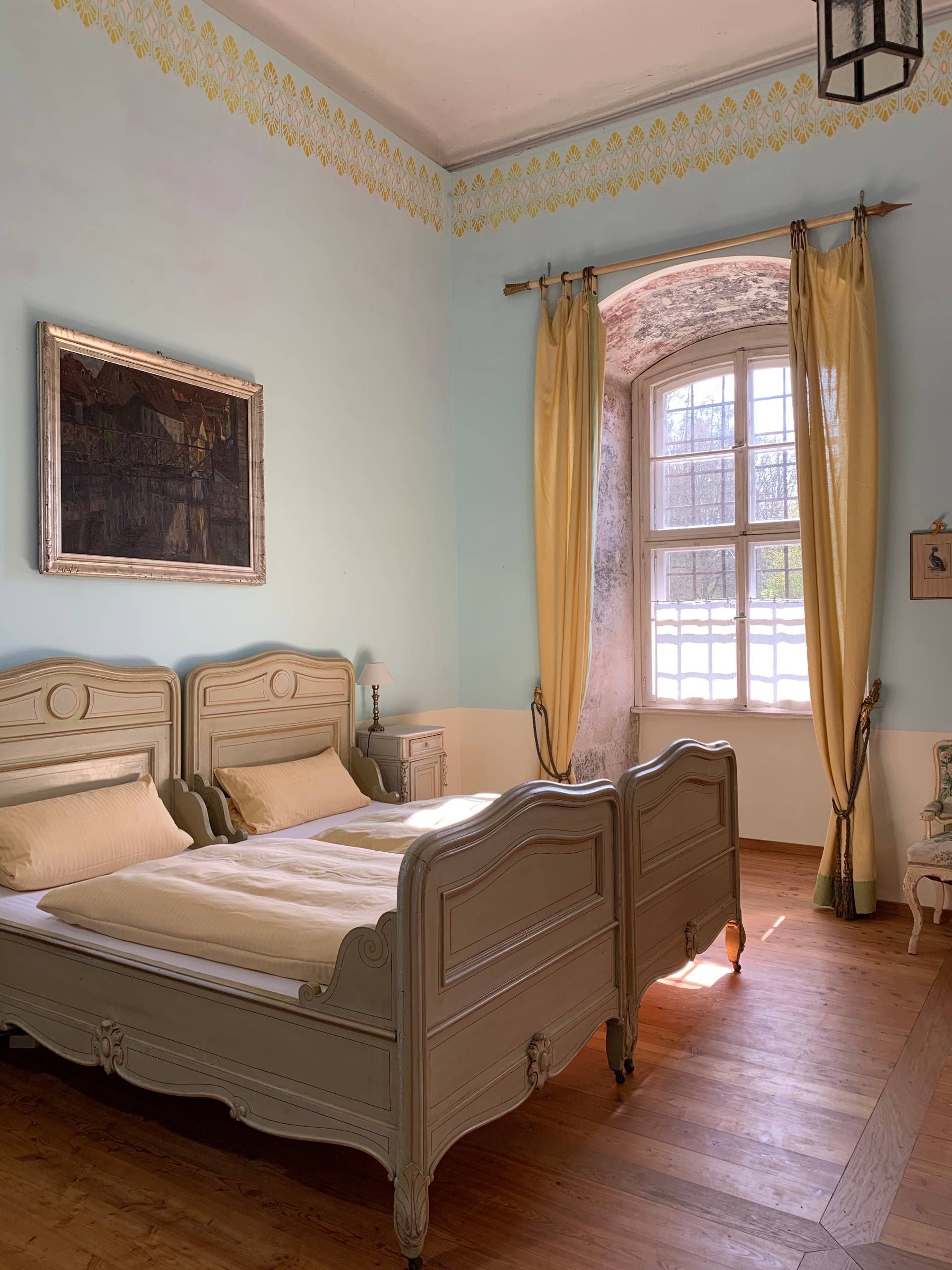 Un dormitorio con una cama grande, una ventana con cortinas, un cuadro en la pared y una lámpara en una mesita de noche.