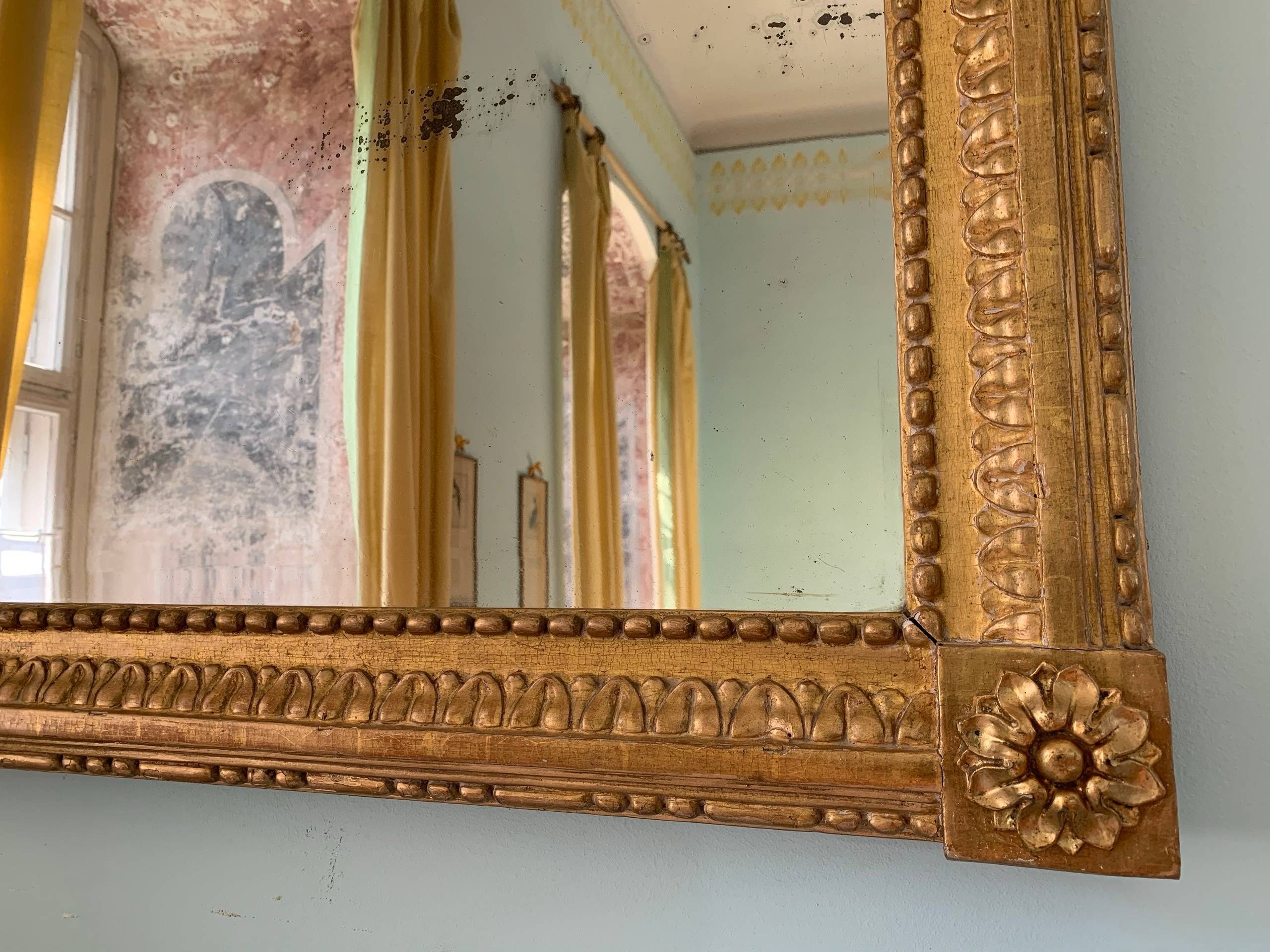 Un miroir orné de motifs dorés et agrémenté d’un décor floral dans le coin inférieur droit.