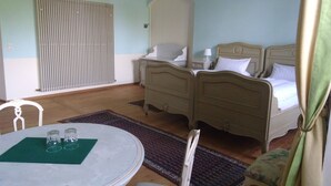A room with two beds, a table with glasses, a radiator, and a patterned rug. - Ferienzimmer im Schloss Burgpreppach (Burgpreppach)